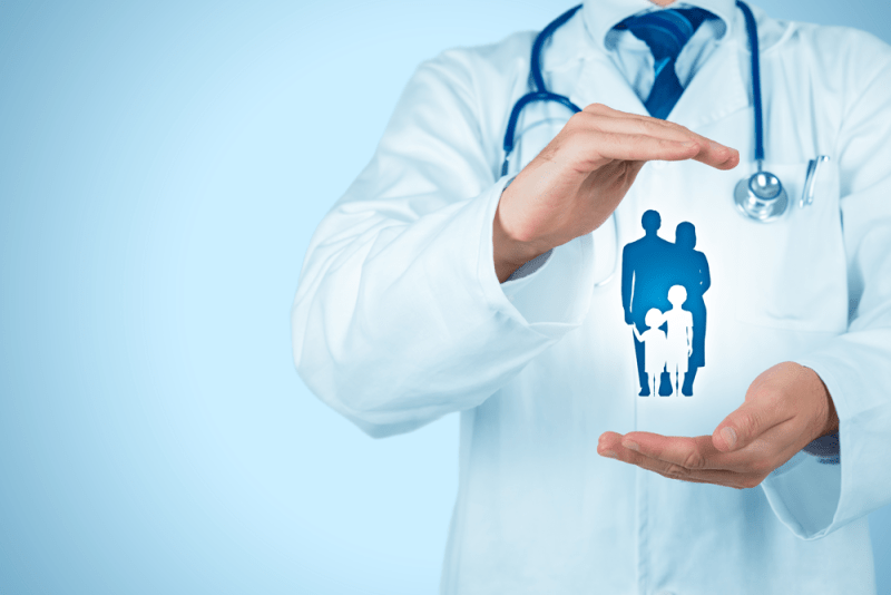 A doctor in a white coat holds a blue silhouette of a family, symbolizing health and care for patients. The image emphasizes family-centered healthcare.