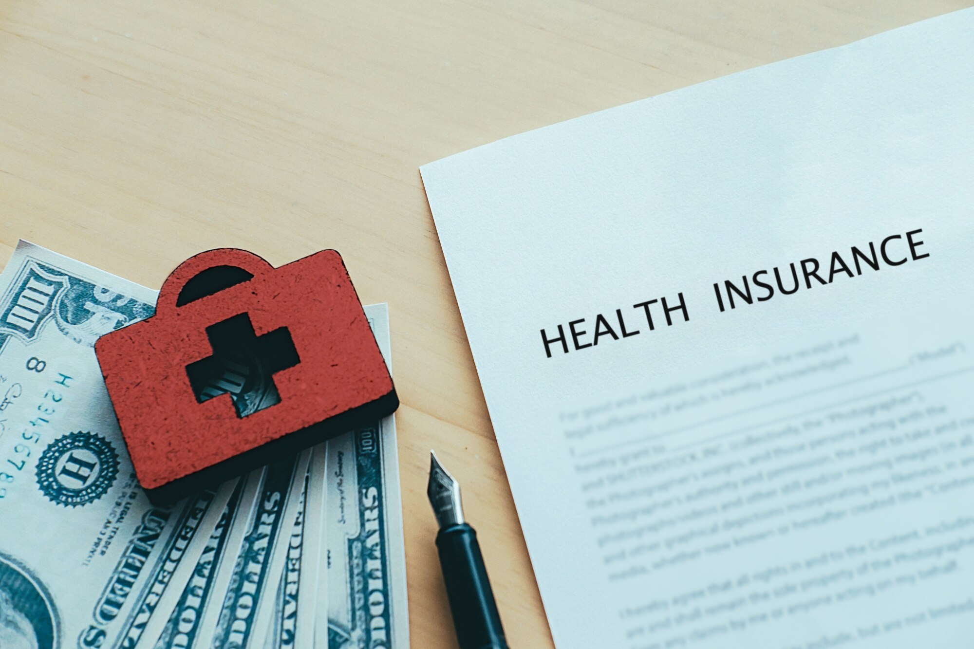 Red and black first aid kit atop cash and a document titled "Health Insurance," symbolizing healthcare costs and insurance options.